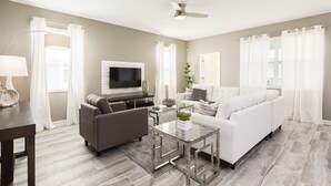 Un salon moderne avec un canapé blanc, une table basse en verre, un téléviseur à écran plat et un ventilateur de plafond.