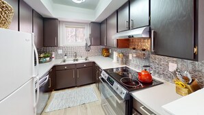 Una cocina moderna con armarios oscuros, encimera blanca, hervidor rojo y pileta de acero inoxidable.