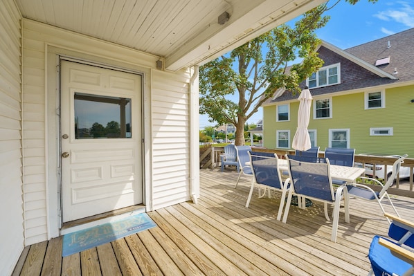 Una terraza de madera con muebles de exterior, una puerta y vistas a casas vecinas.