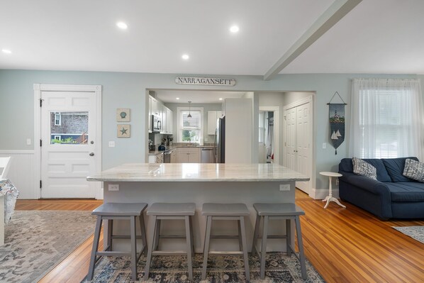 A modern kitchen with a central island, bar stools, and a view into the dining area.