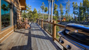 Una terraza de madera con mobiliario exterior y una parrilla, con vistas a una zona boscosa.
