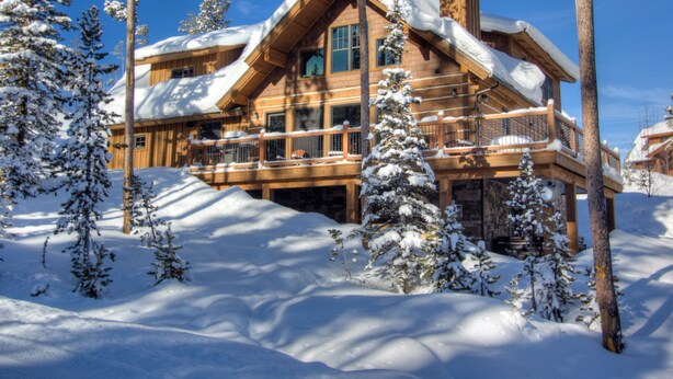 Un amplio lodge de madera con varios balcones y una chimenea, rodeado de árboles cubiertos de nieve.