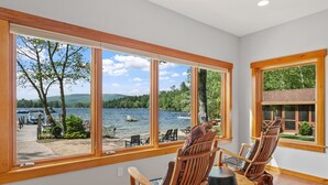 Ein Zimmer mit großen Fenstern und Seeblick, Holzstühle sowie eine Aussicht auf Boote und einen Steg.