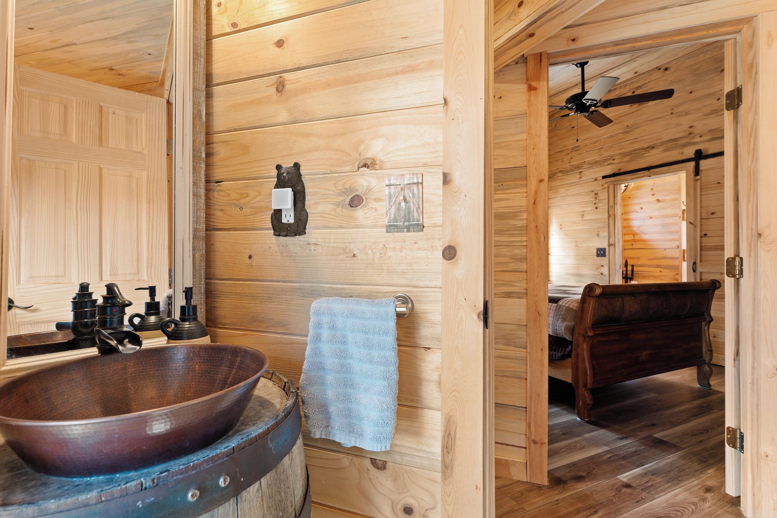Een houten cabin met een grote houten spoelbak, een zeepdispenser in de vorm van een beer, een handdoek, een bed en een plafondventilator.