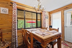 Un intérieur en bois comprenant une table à manger, des chaises, un lustre et une fenêtre avec des rideaux.