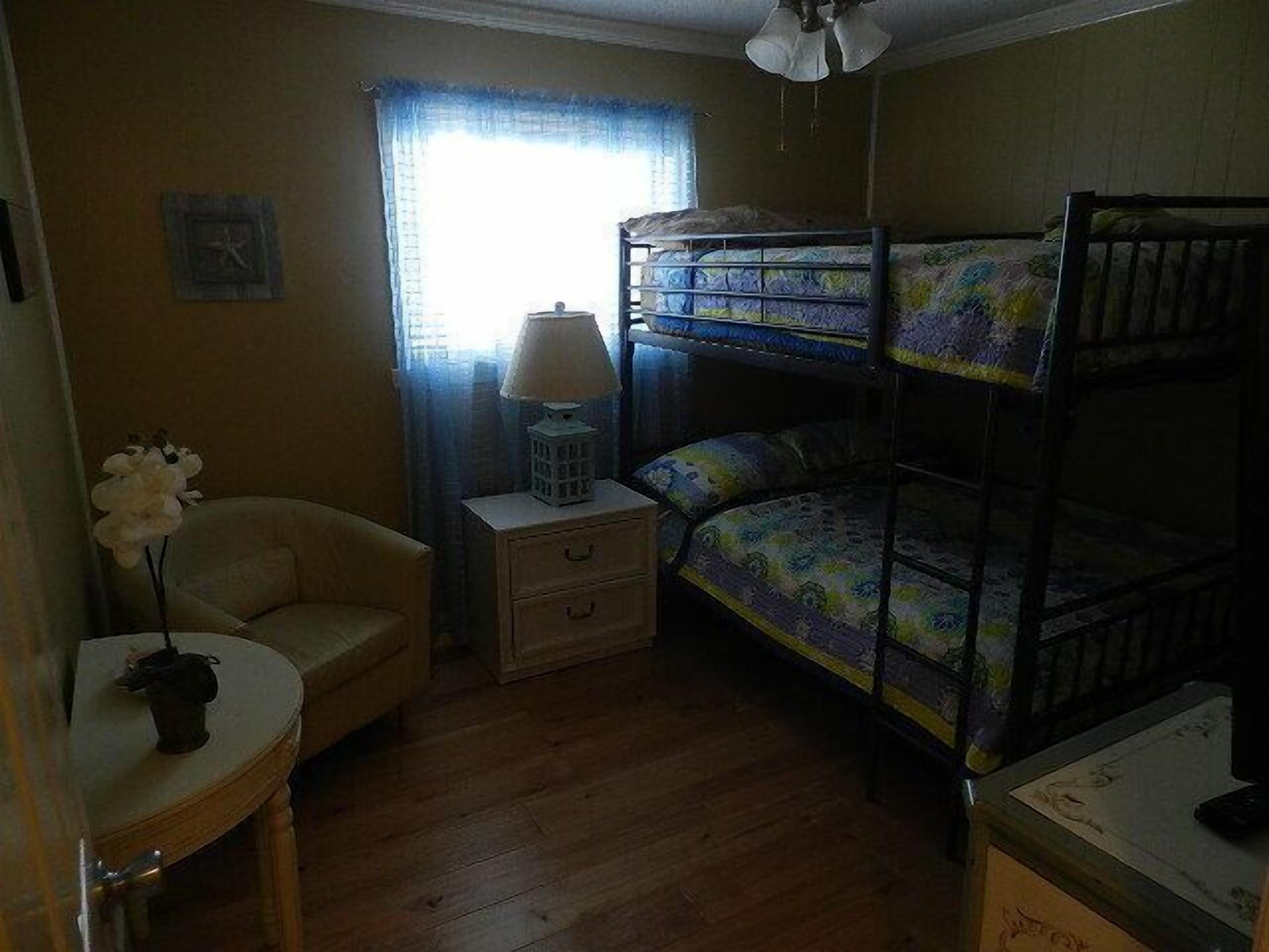 A room with bunk beds, a small table with a lamp, a chair, and a window with curtains.