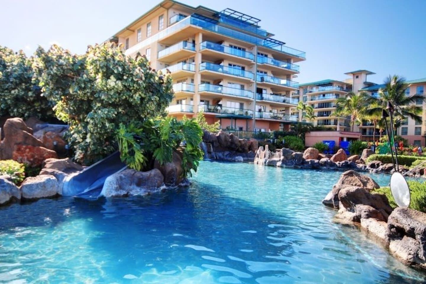 A resort with a swimming pool, a slide, and a multi-story building with balconies.