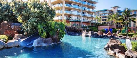 A resort with a swimming pool, a slide, and a multi-story building with balconies.