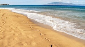 Une plage où l’on voit des empreintes de pas dans le sable, avec une montagne en arrière-plan.