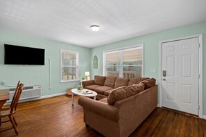 Una sala de estar con un sofá marrón, una mesita, un televisor y una puerta.