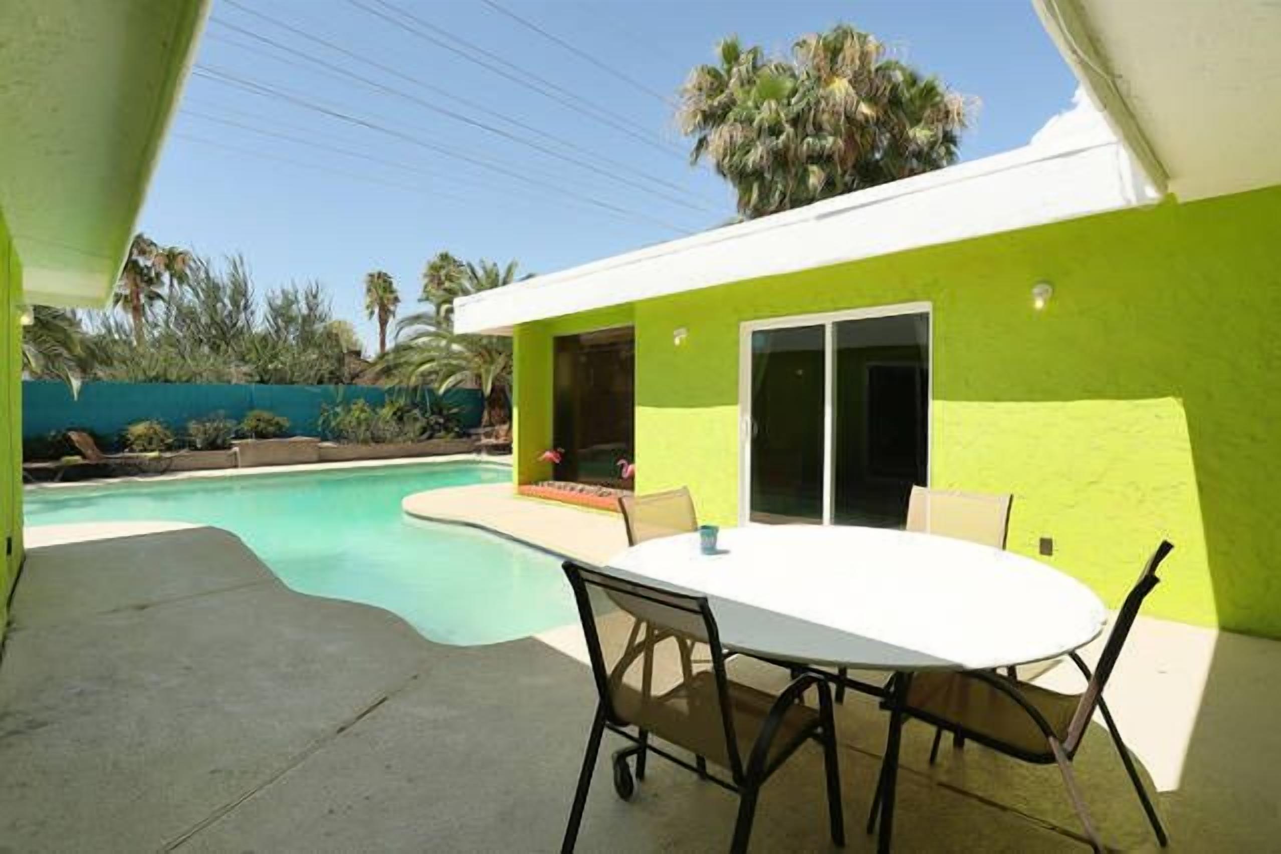 A patio with a table and chairs, a swimming pool, and a building with a bright green exterior.