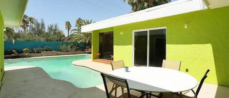 A patio with a table and chairs, a swimming pool, and a building with a bright green exterior.