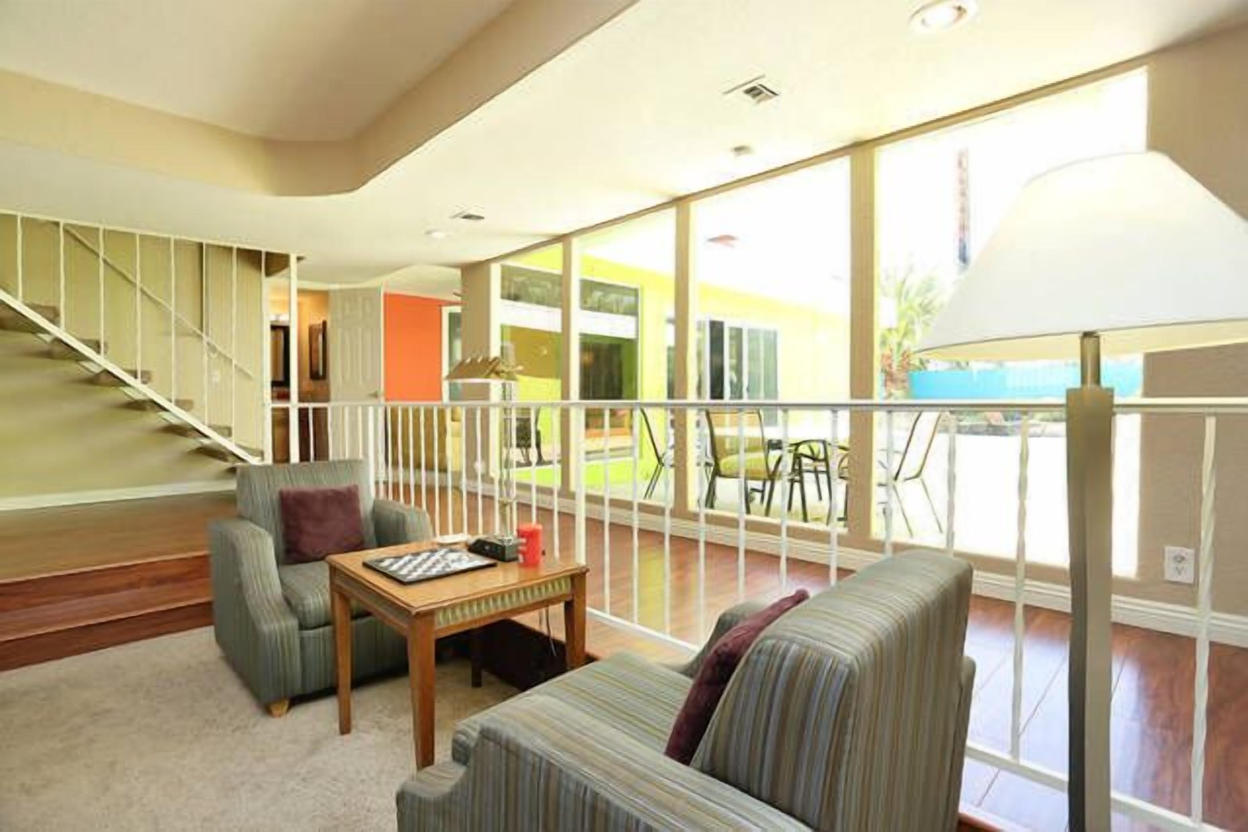 A spacious living room with a staircase, a sofa, a table, and a large window offering a view of the outside.