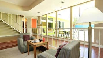 A spacious living room with a staircase, a sofa, a table, and a large window offering a view of the outside.
