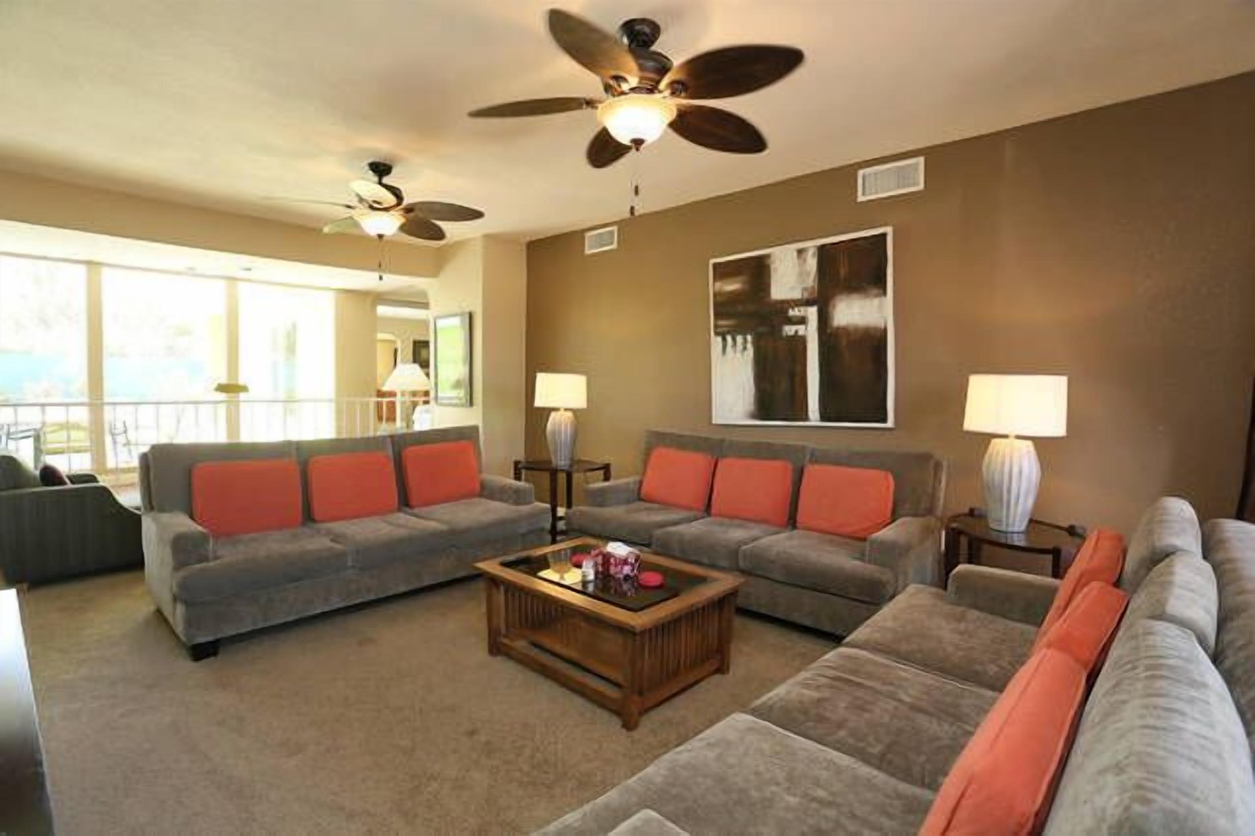 A spacious living room with two sofas, a coffee table, and ceiling fans.