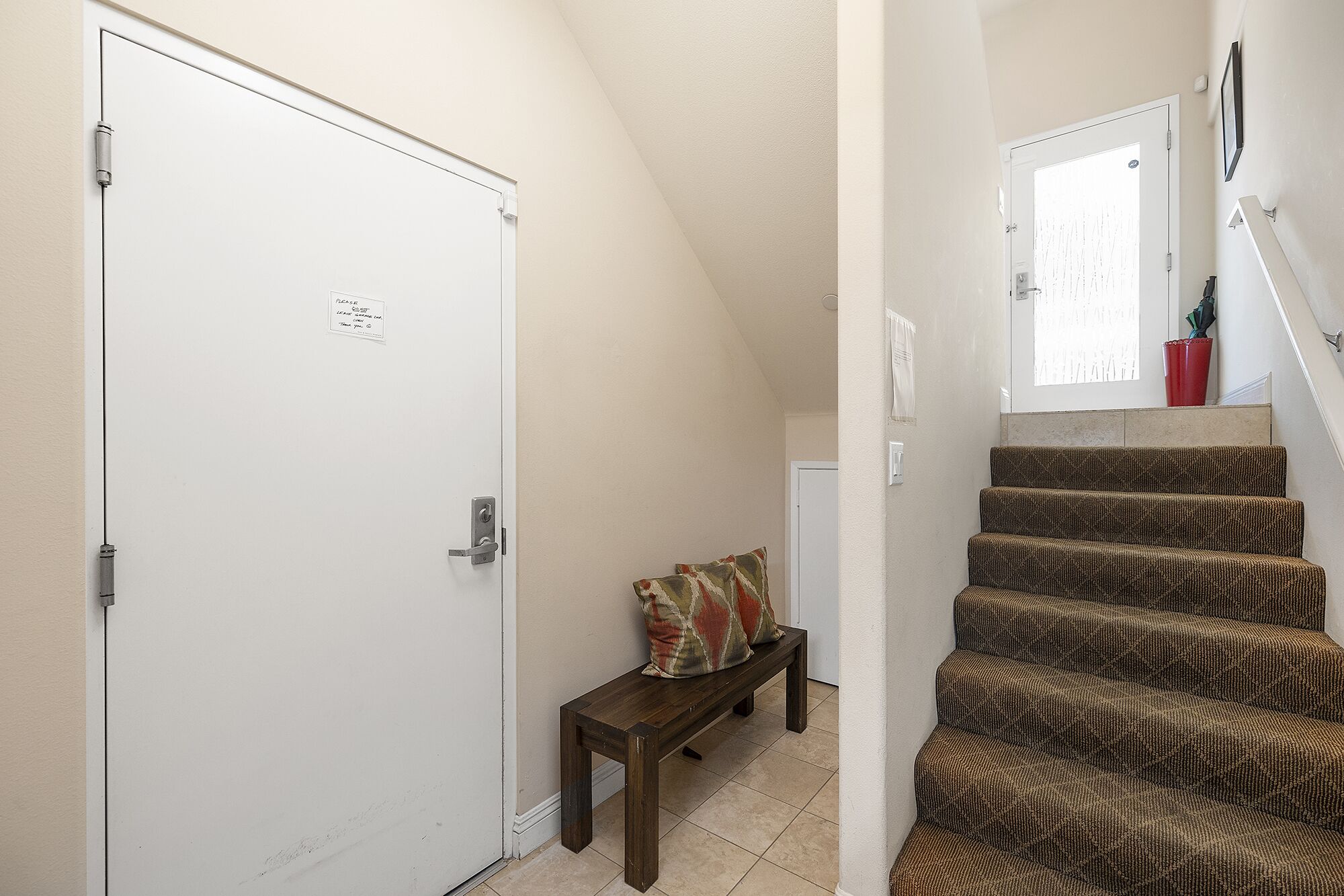 A staircase with patterned carpet, a wooden bench, and a white door with a sign.