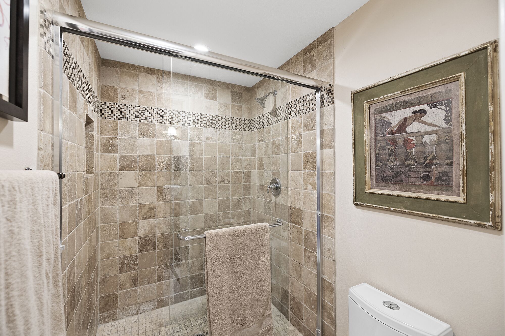 Una ducha con puerta de vidrio, paredes con azulejos y un cuadro en la pared.