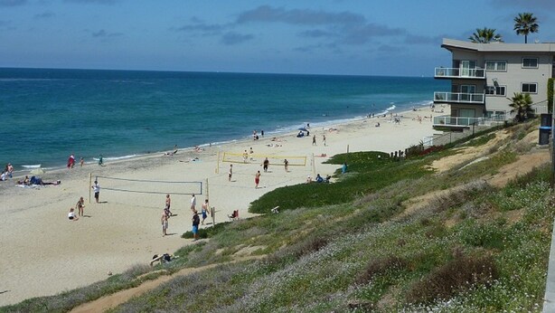 A beach with a volleyball net, people, and a building with balconies. - Spacious Village beach house. Private rooftop deck. Walk to beaches and shops.  (Carlsbad)