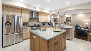 A modern kitchen with stainless steel appliances, wooden cabinets, a central island, and a dining area with a chair and table. - Spacious Village beach house. Private rooftop deck. Walk to beaches and shops.  (Carlsbad)