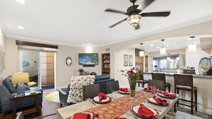 A dining area with a long table set for six, a ceiling fan, and a kitchen in the background. - Spacious Village beach house. Private rooftop deck. Walk to beaches and shops.  (Carlsbad)