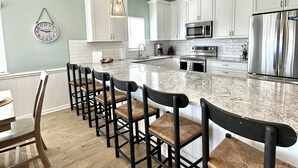 A modern kitchen with white cabinets, a large island, bar stools, and a hanging light fixture. - OCEAN FRONT with POOL, Great LOCATION near pier, 5 bed & 5 bath (Ocean Isle Beach)