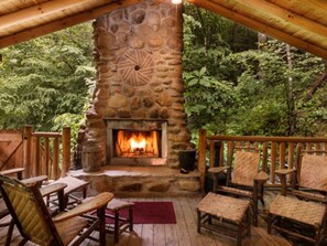 A stone fireplace with a fire, surrounded by wooden furniture and a wooden deck.