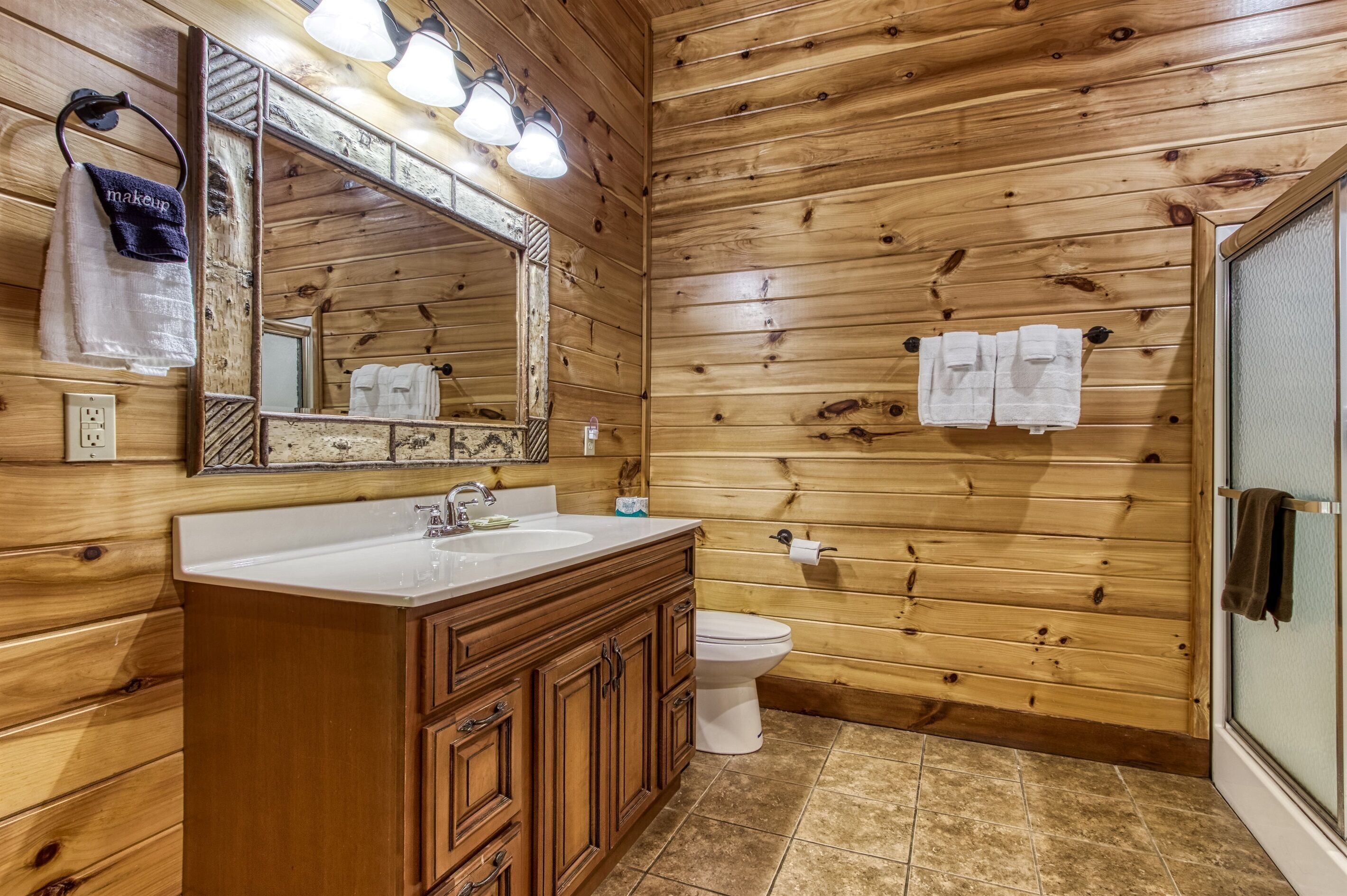Ein Badezimmer mit Holzvertäfelung, einem Waschbecken, einem Spiegel und einer Toilette.