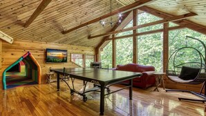 A wooden interior with a ping pong table, a red sofa, and a hanging chair. - RIVERFRONT LUXURY LODGE/4 KING SUITES/Swim Spa/Game Room/Fire Pit/4,200 Sq. Ft. (Sevierville)