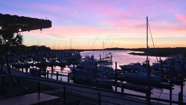 Un port de plaisance au crépuscule, avec des bateaux amarrés, une jetée en bois et une vue sur l’eau.