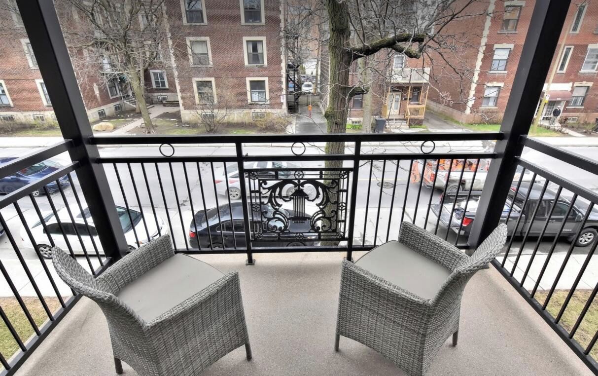 Een balkon met twee rieten stoelen en een metalen hekwerk.