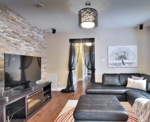 Ein modernes Wohnzimmer mit einer Wand aus Stein, einem Flachbildfernseher, einem schwarzen Ledersofa und einem gemusterten Teppich.