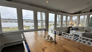 Una habitación amplia con grandes ventanales con vista a un lago, una mesa de madera con adornos y una zona de estar acogedora con un tapete estampado.