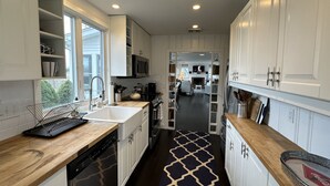 Una cocina moderna con armarios blancos, encimera de madera, alfombra estampada en blanco y negro, y vistas al salón.