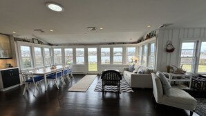 Amplia sala de estar con un gran ventanal con vistas a un lago, comedor con mesa y sillas de madera, y una zona de estar acogedora con un tapete estampado.