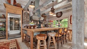 A rustic kitchen with wooden bar stools, a large island, and a refrigerator. - LUXURY 4 Kng Bdrm, 4.5 Bth, Gourmet Kitchen, Pavilion; TV, Fire Place, Heaters (Asheville)