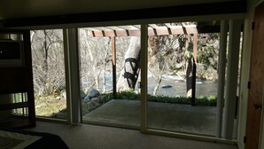 A room with a sliding glass door leading to a covered outdoor area with a view of a river and trees. - Riverfront North Fork Kaweah - 1500 Ft of your own river! (Three Rivers)