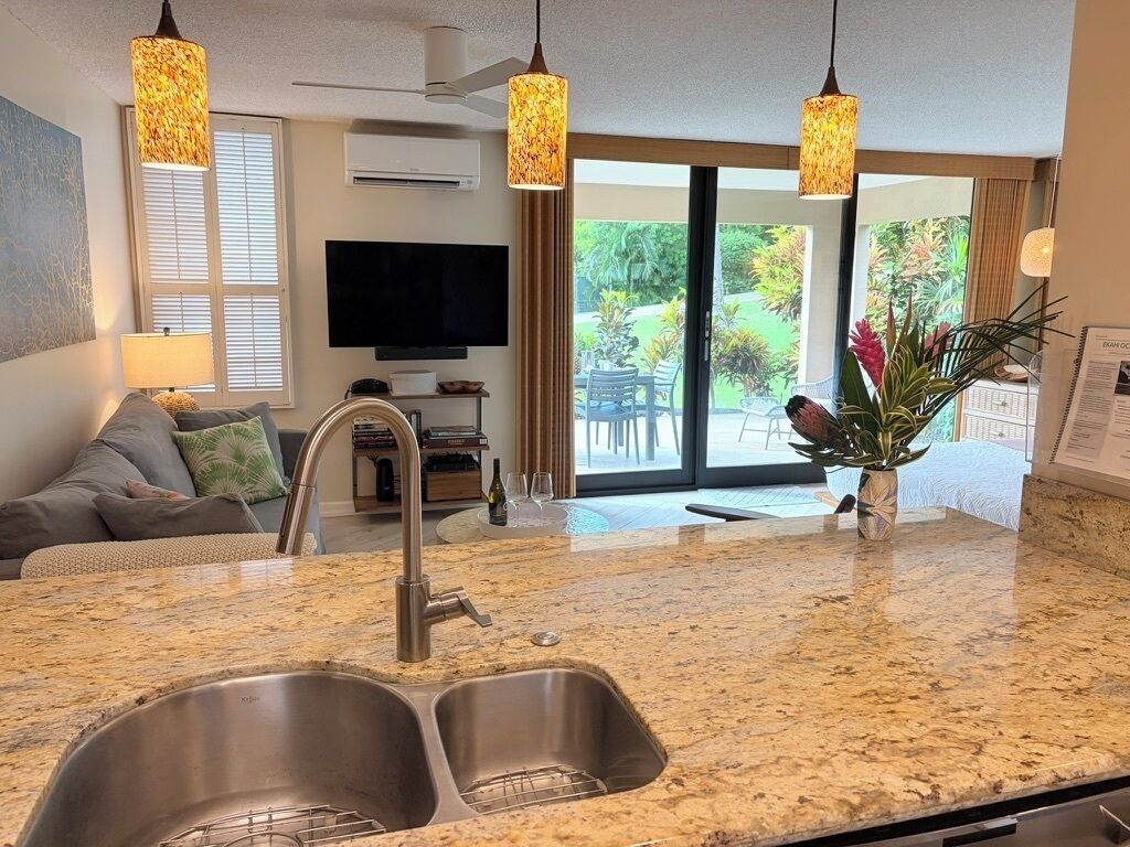 A modern kitchen with a granite countertop, stainless steel sink, and pendant lighting.