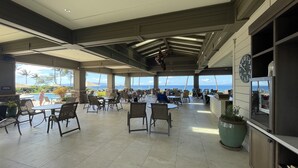 Un vaste espace intérieur doté de nombreuses tables et chaises, de grandes fenêtres donnant sur l’océan et d’une horloge au mur.