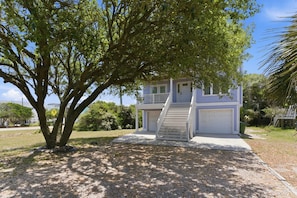 A two-story house with a front porch, a driveway, and a large tree in the foreground.