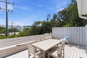 An outdoor deck with a wooden table and chairs, a white fence, and a view of buildings and trees.