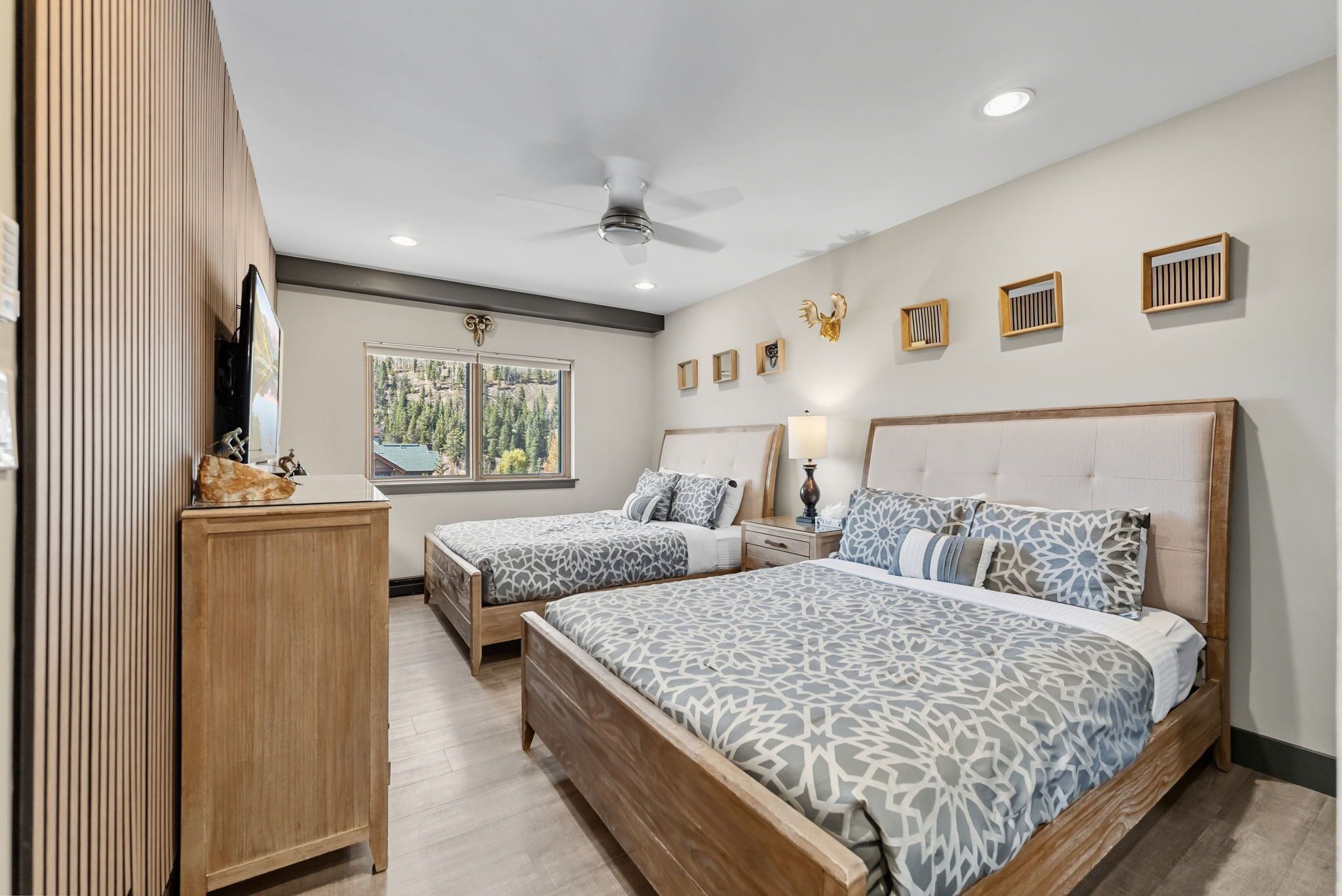 A bedroom with two beds, a ceiling fan, a window with a view, and wall-mounted decor.
