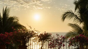 A sunset view from a balcony with potted plants and a railing overlooking the sea.