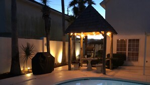 A pool area with a gazebo, palm trees, and a patio with outdoor furniture.