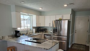 A modern kitchen with white cabinets, stainless steel appliances, a marble countertop, and wooden stools.