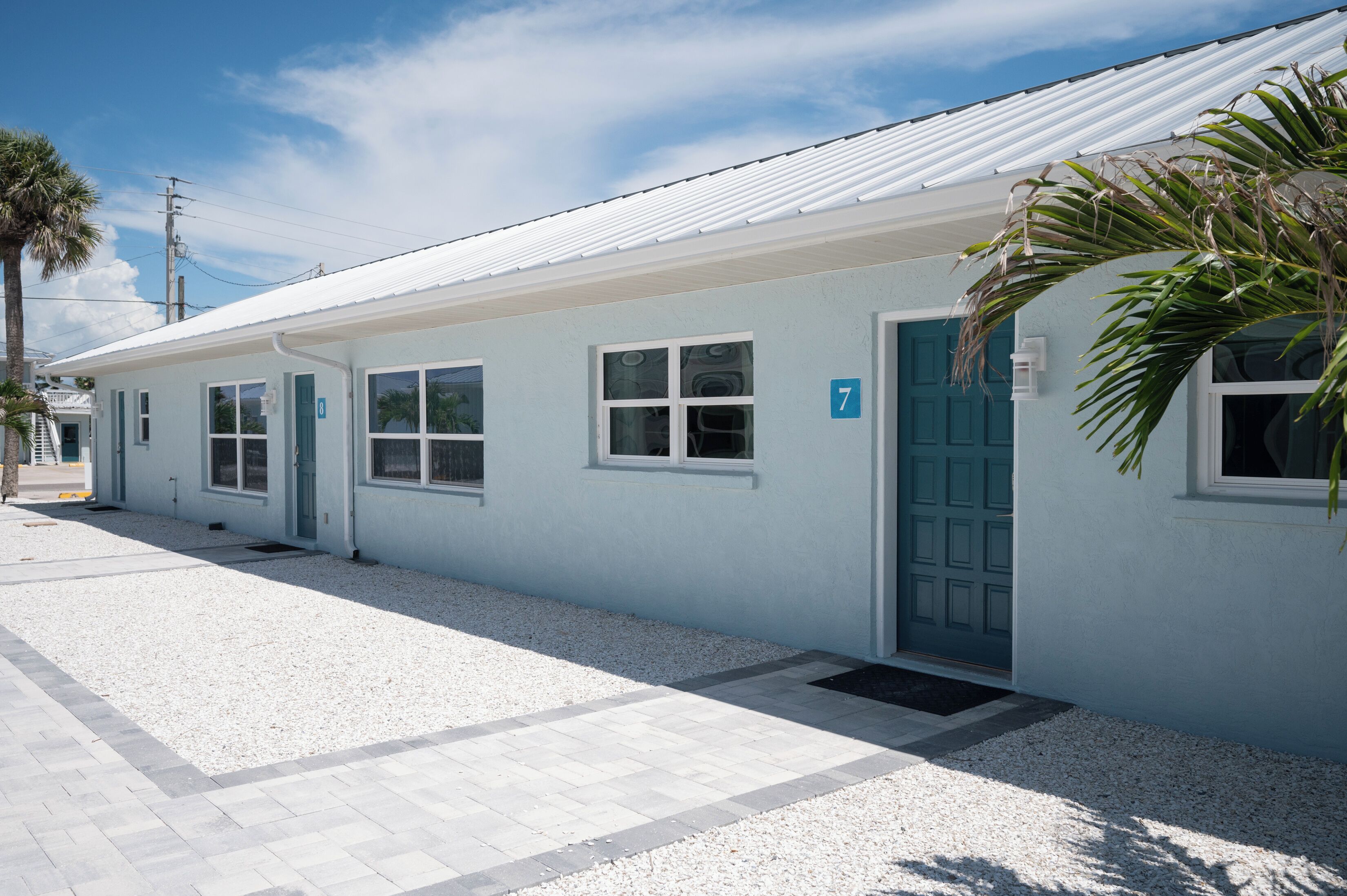 A single-story building with a light blue exterior, numbered 7, featuring a blue door and windows.