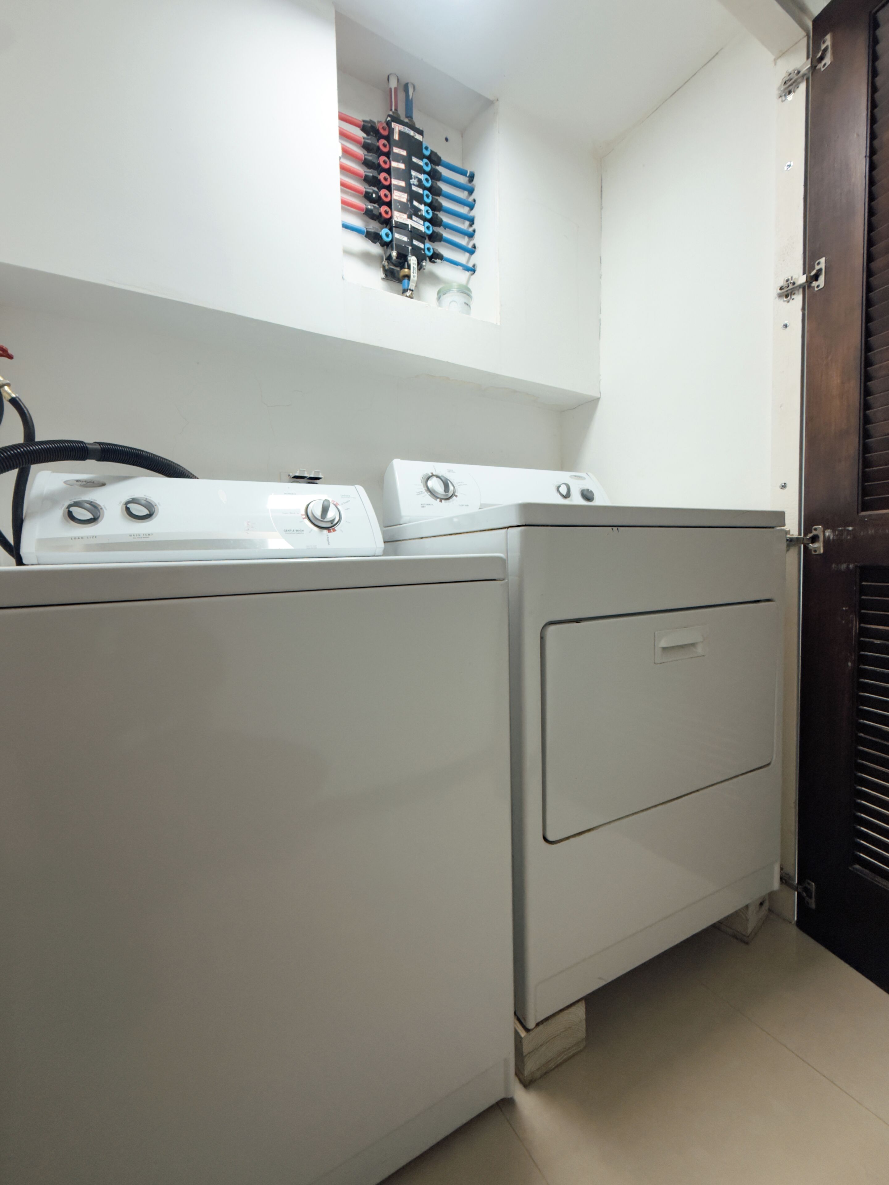 A laundry area with a washer and dryer, a wall-mounted hose reel, and a door.