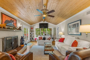 A spacious living room with a fireplace, white sofas, a coffee table, and a ceiling fan.