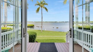 Eine offene Veranda mit Blick auf ruhiges Wasser, Palmen und eine Rasenfläche.