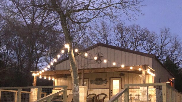 A rustic building with a wooden staircase leading to a covered porch, string lights, and outdoor seating. - Hidden Piece of Heaven on Lake Limestone (Thornton)