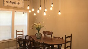 A dining area with a wooden table and chairs, a hanging light fixture with multiple bulbs, and a sign on the wall that reads "THIS IS OUR HAPPY PLACE". - Hidden Piece of Heaven on Lake Limestone (Thornton)